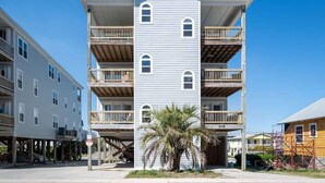 A multi-story building with balconies, a palm tree in front, and a clear blue sky.
