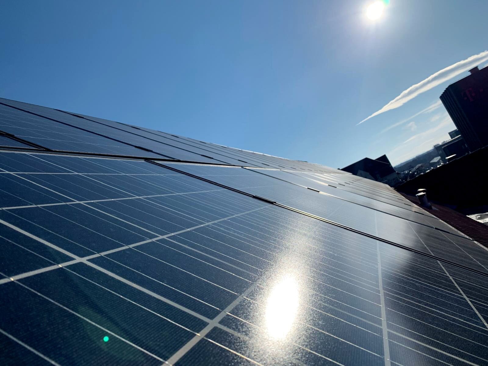 A close-up of solar panels with a clear sky and a building in the background.