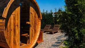 Una cabaña de madera con un amplio ventanal circular, mobiliario exterior y un camino de grava.