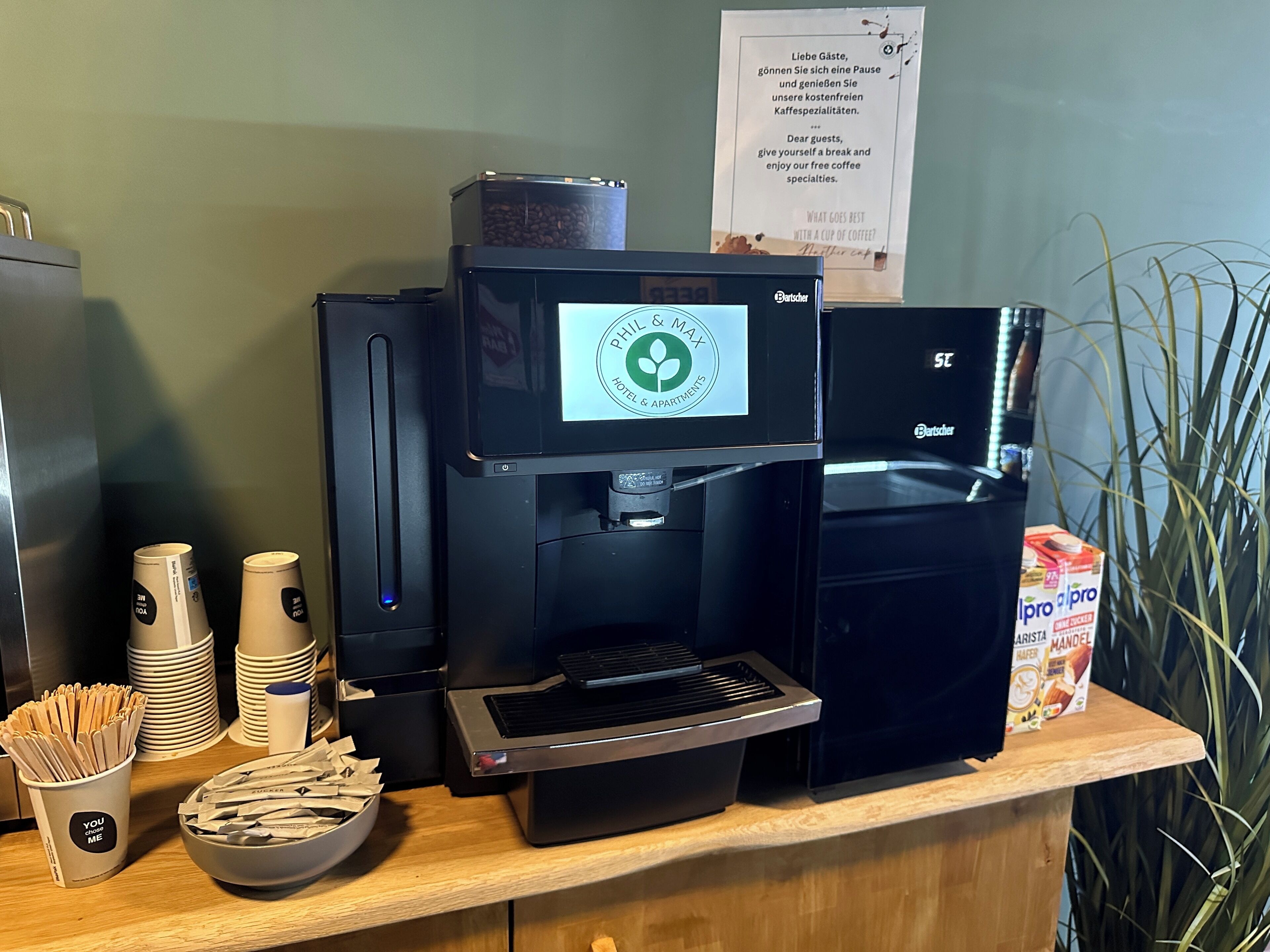 A coffee station with a coffee machine, disposable cups, and a bowl of sugar packets.