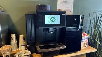 A coffee station with a coffee machine, disposable cups, and a bowl of sugar packets.