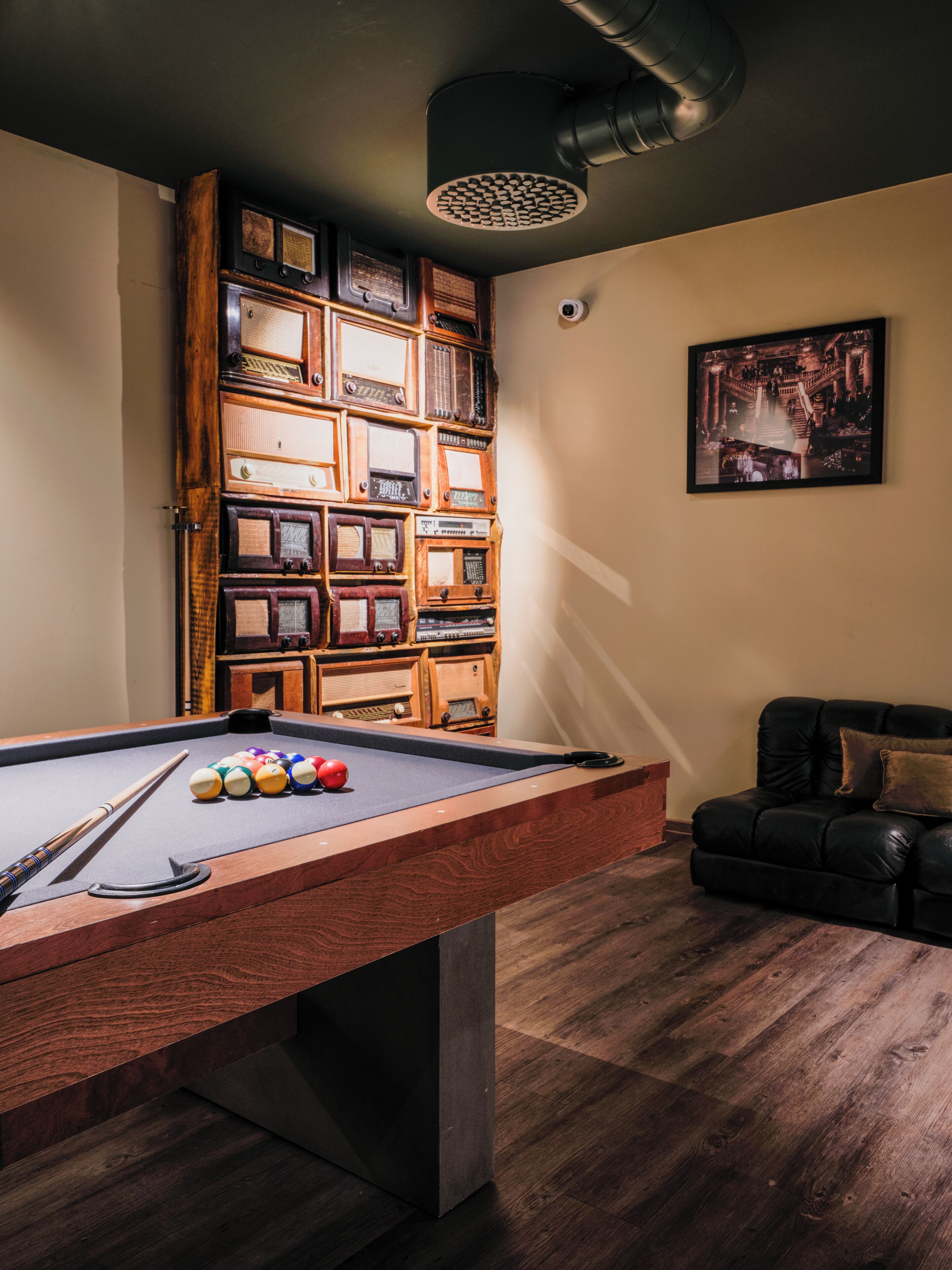 Ein Billardtisch mit Kugeln, eine Holzkabine mit Vintage-Radios, ein Ledersofa und ein gerahmtes Bild an der Wand.