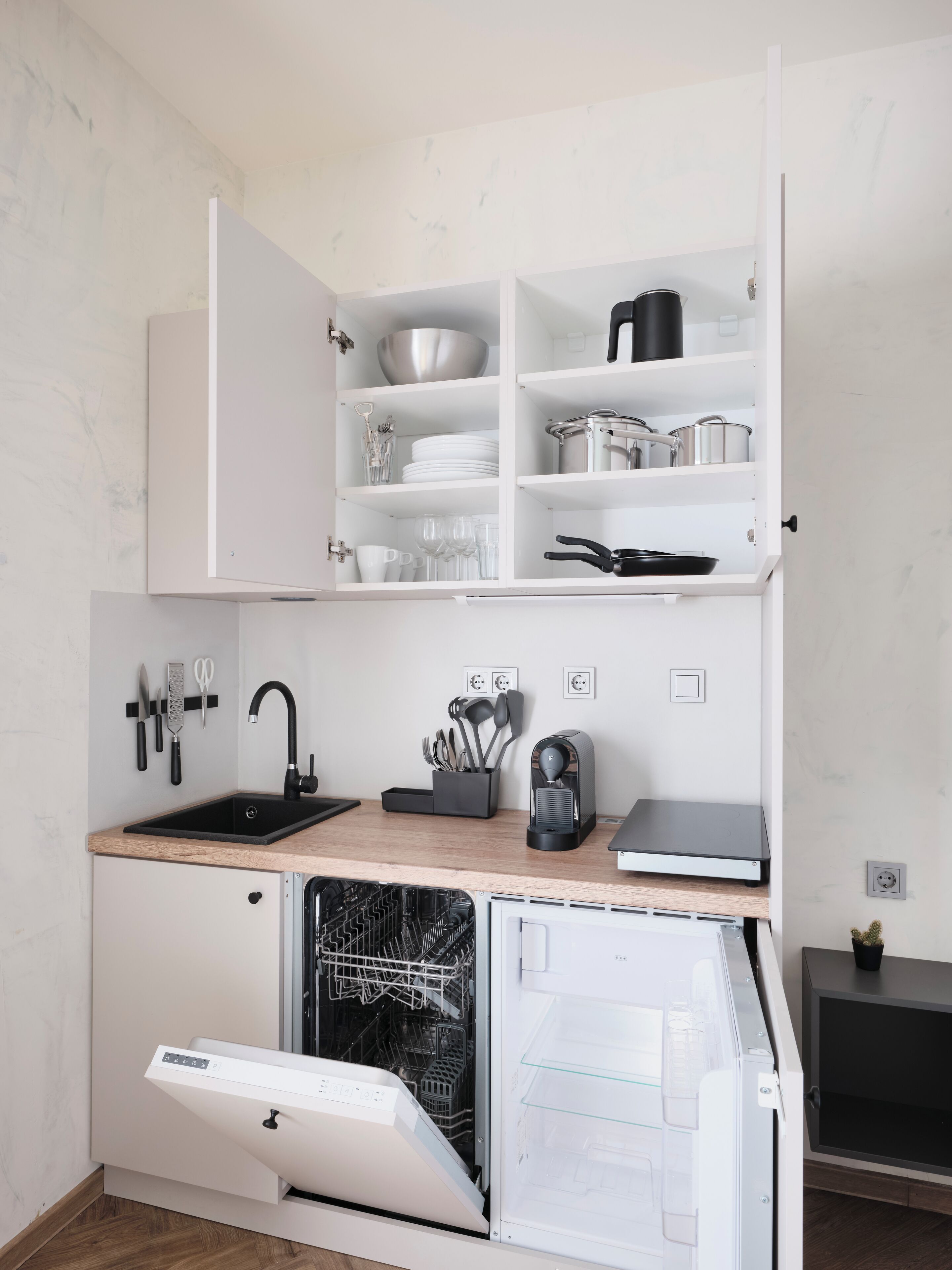 A compact kitchen with white cabinetry, a black sink, and a dishwasher.