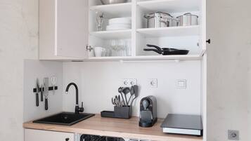 Cocina compacta con armarios blancos, un lavamanos negro y un lavavajillas.