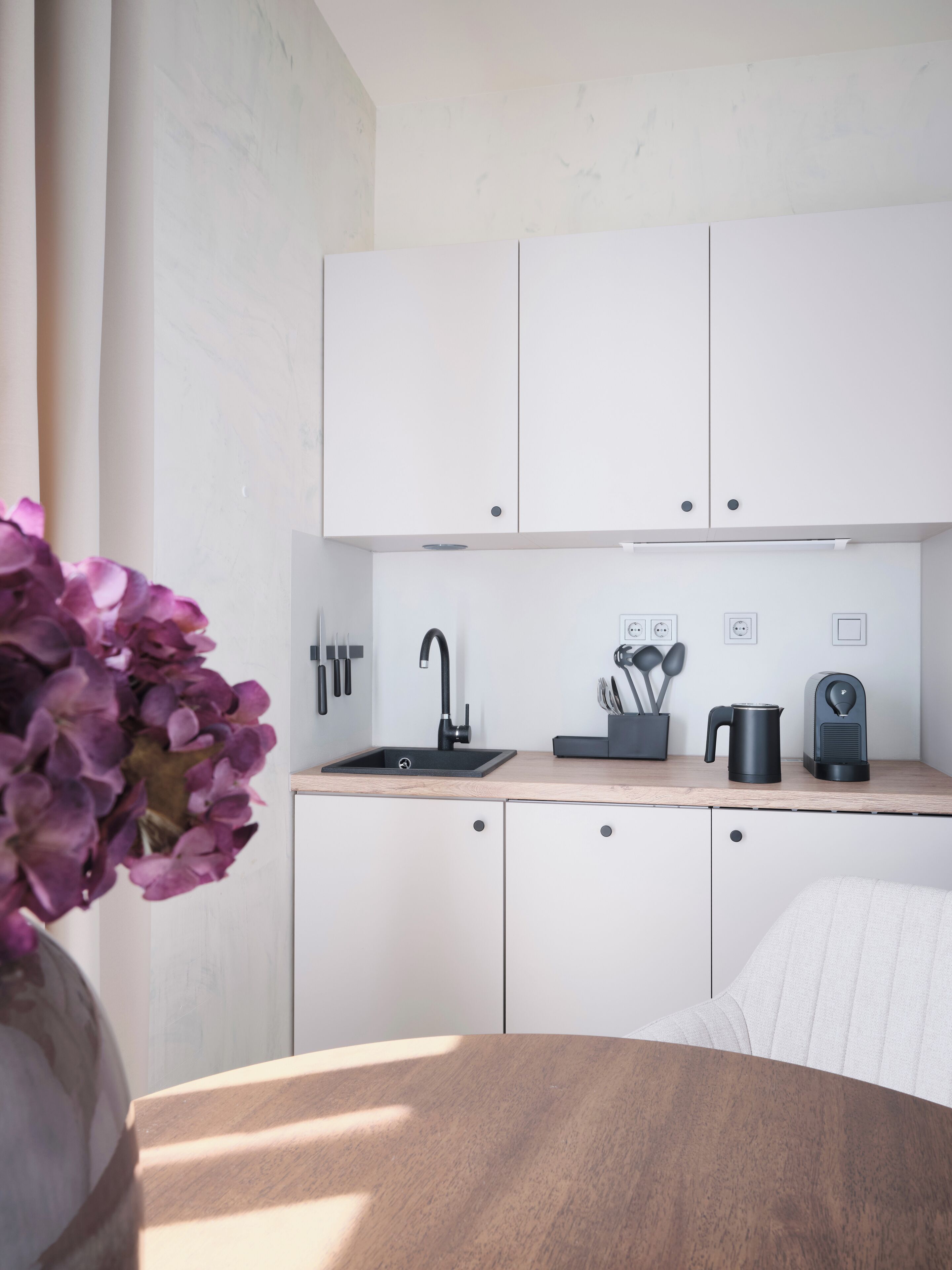 Een moderne keuken met witte kastjes, een zwarte spoelbak en een koffieapparaat.