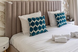 Een net opgemaakt bed met witte lakens, twee gestreepte kussens en een nachtkastje met een lamp en een zakdoosje.