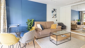 Ett modernt vardagsrum med en blå accentvägg, en beige soffa, ett soffbord i glas och en gul stol.