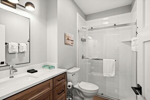 Et moderne badeværelse med en hvid vask, trækommode, toilet og brusekabine med glasvægge.