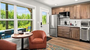 A modern kitchen with wooden cabinets, stainless steel appliances, and a view of greenery through large windows. - RiverWest Hunters Landing - Hot Tub - Riverfront - Dogs (Duluth)