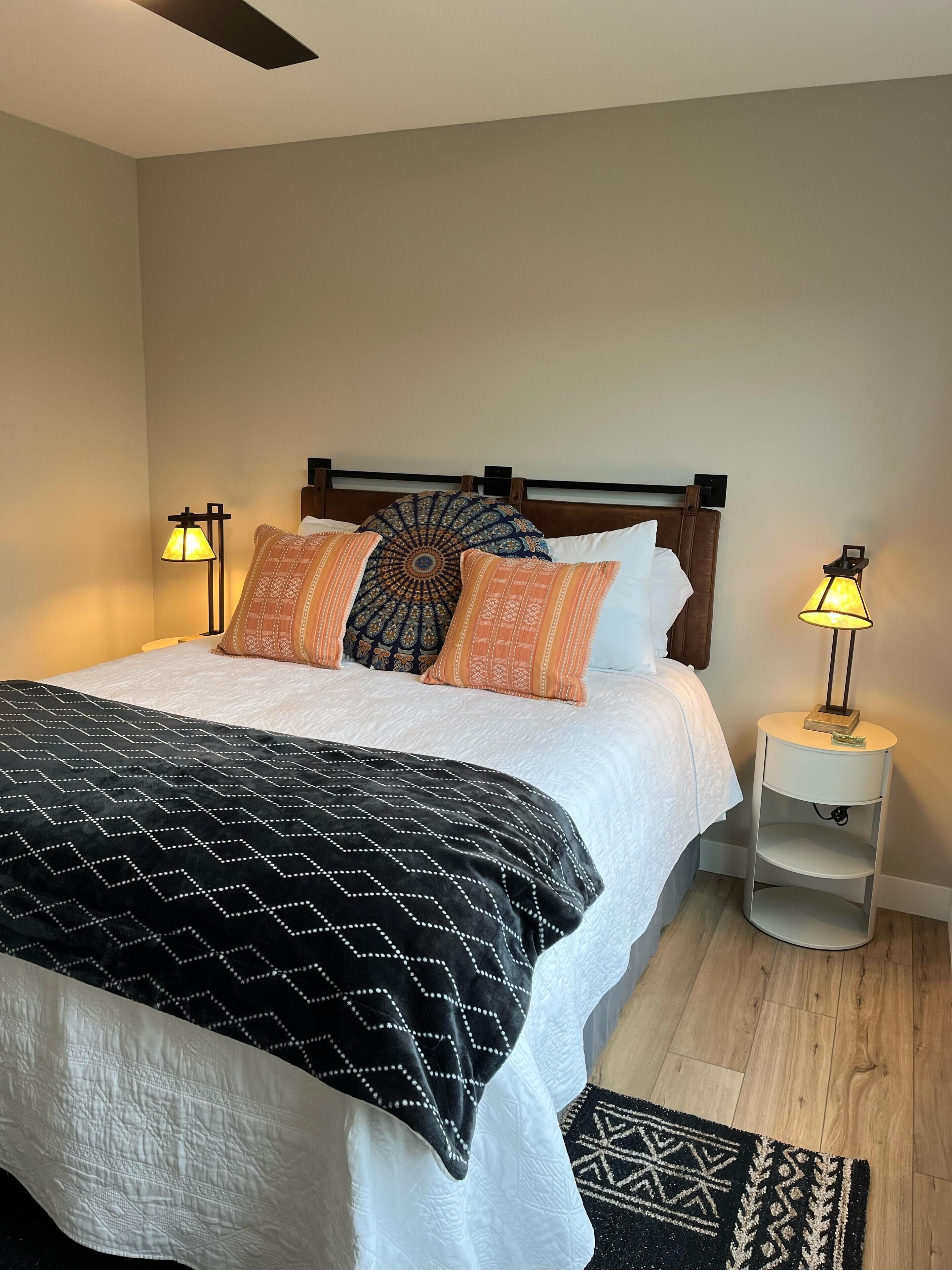 Een net opgemaakt bed met gestreepte kussens en een zwart-wit deken, met aan beide zijden nachtkastjes en lampen.
