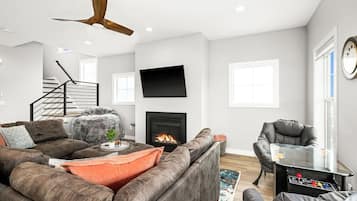 Un salon moderne avec un canapé d’angle, une cheminée, un téléviseur fixé au mur et un ventilateur de plafond.