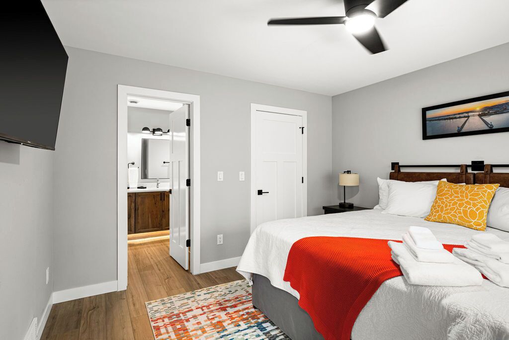 A hotel room with a bed, a nightstand, a TV mounted on the wall, and a door leading to a bathroom.