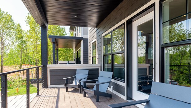 Una terraza de madera con asientos exteriores y grandes ventanas con vistas a un jardín.