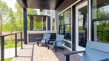 Une terrasse en bois avec des sièges extérieurs et de grandes fenêtres donnant sur un jardin.