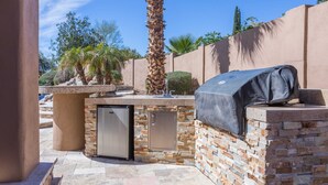 A patio with a grill, a refrigerator, and a stone wall. - Desert Paradise, Pool, Spa, Pickleball, Putt Green (Phoenix)