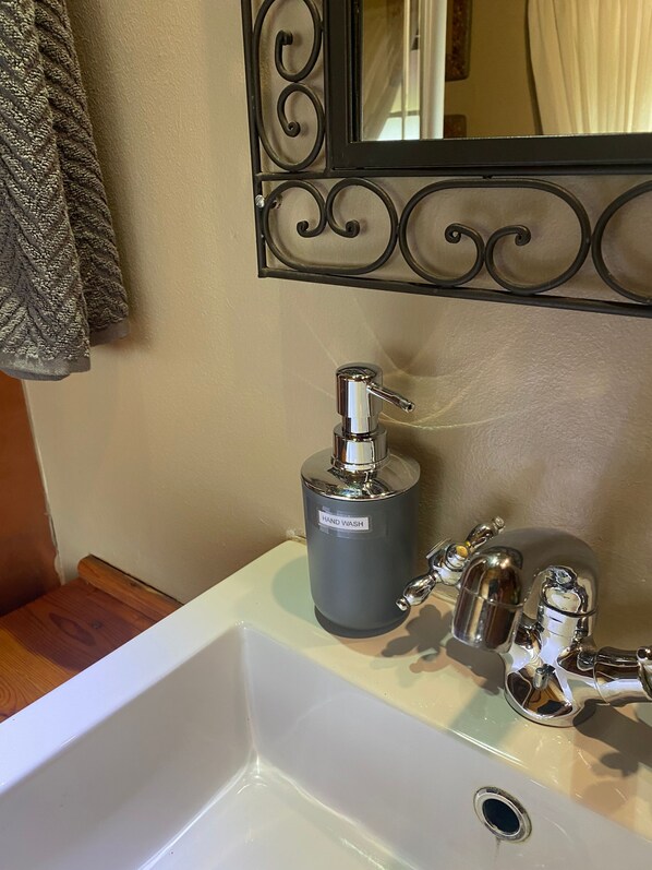 Un baño con un lavabo blanco, dispensador de jabón para manos y un espejo con marco decorativo.