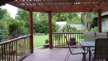 Una terraza de madera con una pérgola, mobiliario exterior y vistas a un jardín cuidado.