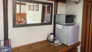 Une pièce avec un plafond en bois, un téléviseur fixé au-dessus d’un réfrigérateur, un four à micro-ondes posé sur le réfrigérateur, une bouilloire et un miroir encadré accroché au mur.