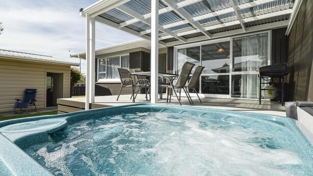 Un espace avec un bain à remous, doté d’un patio couvert, de sièges extérieurs et offrant une vue sur la maison.