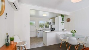 Une cuisine moderne avec des meubles blancs, un îlot central et un coin repas comprenant une table en verre et des chaises blanches.
