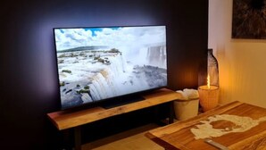 Ein Flachbildfernseher an einem Holzständer, ein Tisch mit einer lederähnlichen Oberfläche und eine Kerze in einem Glasgefäß.