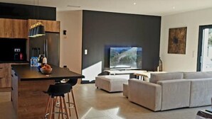 Eine moderne Küche mit Kochinsel, Essbereich inklusive Sofa und einem großen Fernseher.