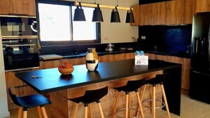 Eine moderne Küche mit einer zentralen Kochinsel, Barhocker, einem schwarzen Kühlschrank und Holzschränken.
