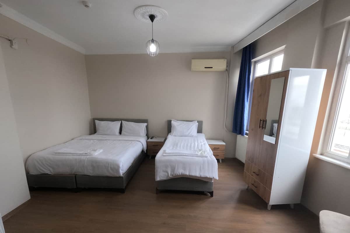 A hotel room with two beds, a wooden wardrobe, a mirror, and a ceiling light.