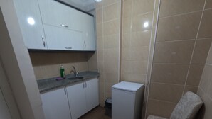 A compact kitchen with white cabinets, a small sink, a refrigerator, and two grey armchairs. - MS kuba Istanbul apart (Istanbul)