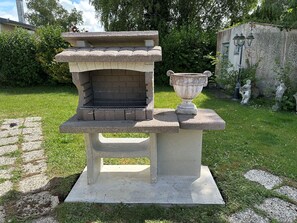 A stone barbecue grill with a decorative urn on a pedestal, set in a grassy garden area. - Quiet Holiday Home Near Authie Bay in Fort-Mahon-Plage (Fort-Mahon-Plage)