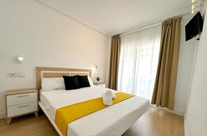 Ein Hotelzimmer mit Bett, Nachttisch, Fernseher und einem Fenster mit Vorhängen.