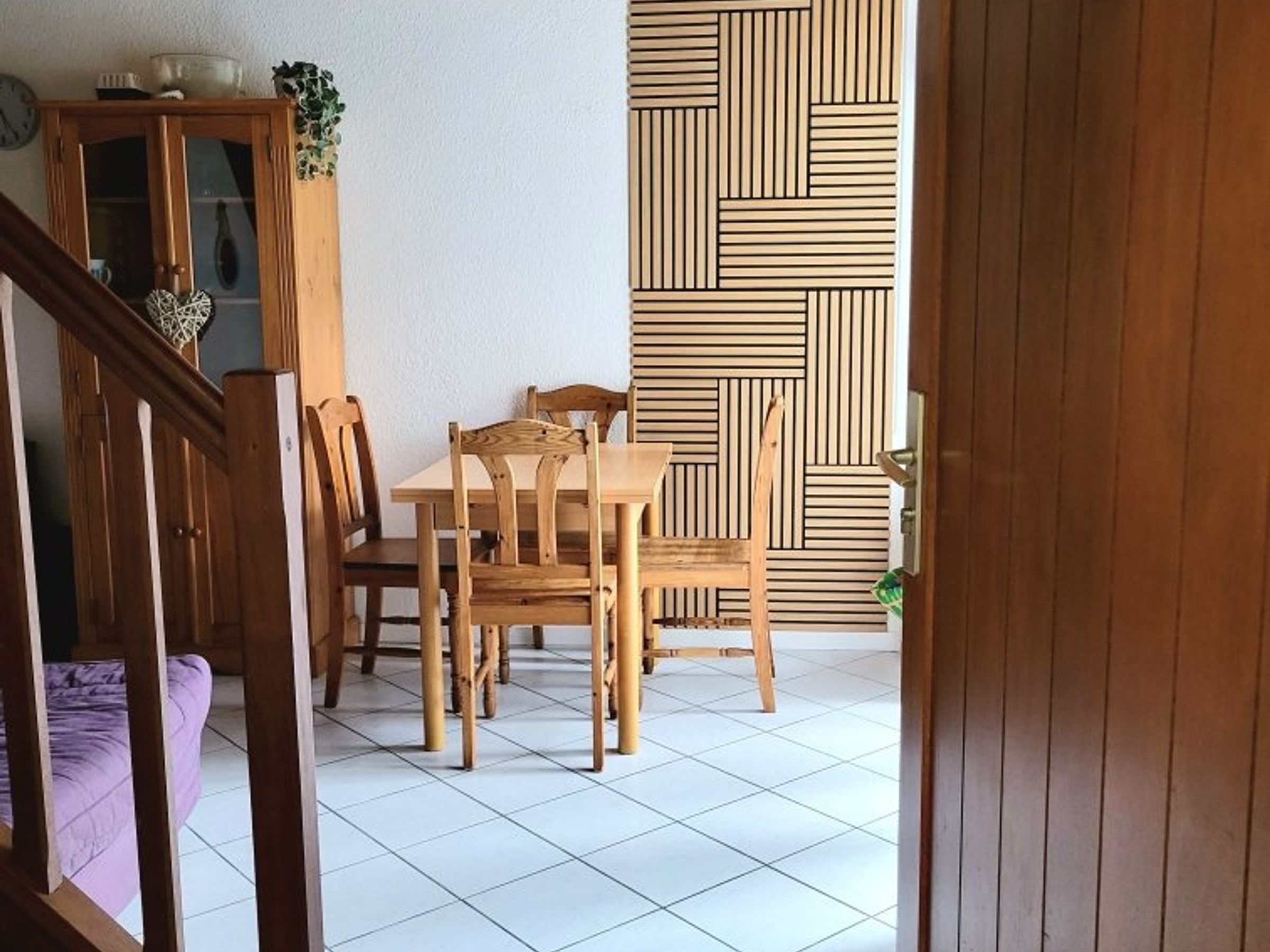 Un comedor con una mesa y sillas de madera, un aparador con puertas de cristal y un papel tapiz estampado.