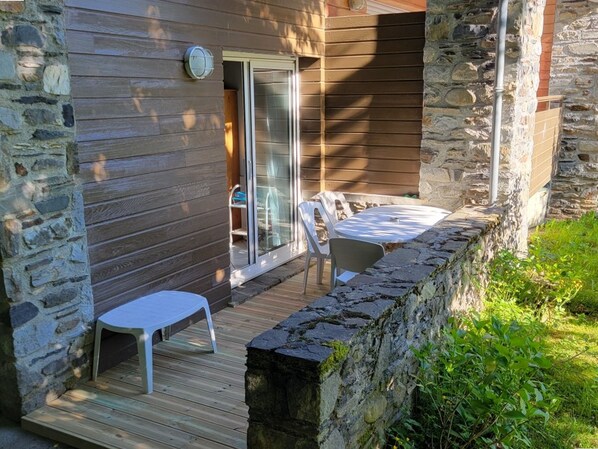 Un espace patio doté d’une terrasse en bois, de murs en pierre et d’une porte vitrée donnant sur un espace intérieur.