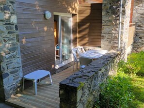 Un patio con terraza de madera, muros de piedra y una puerta de vidrio que da a un espacio interior.