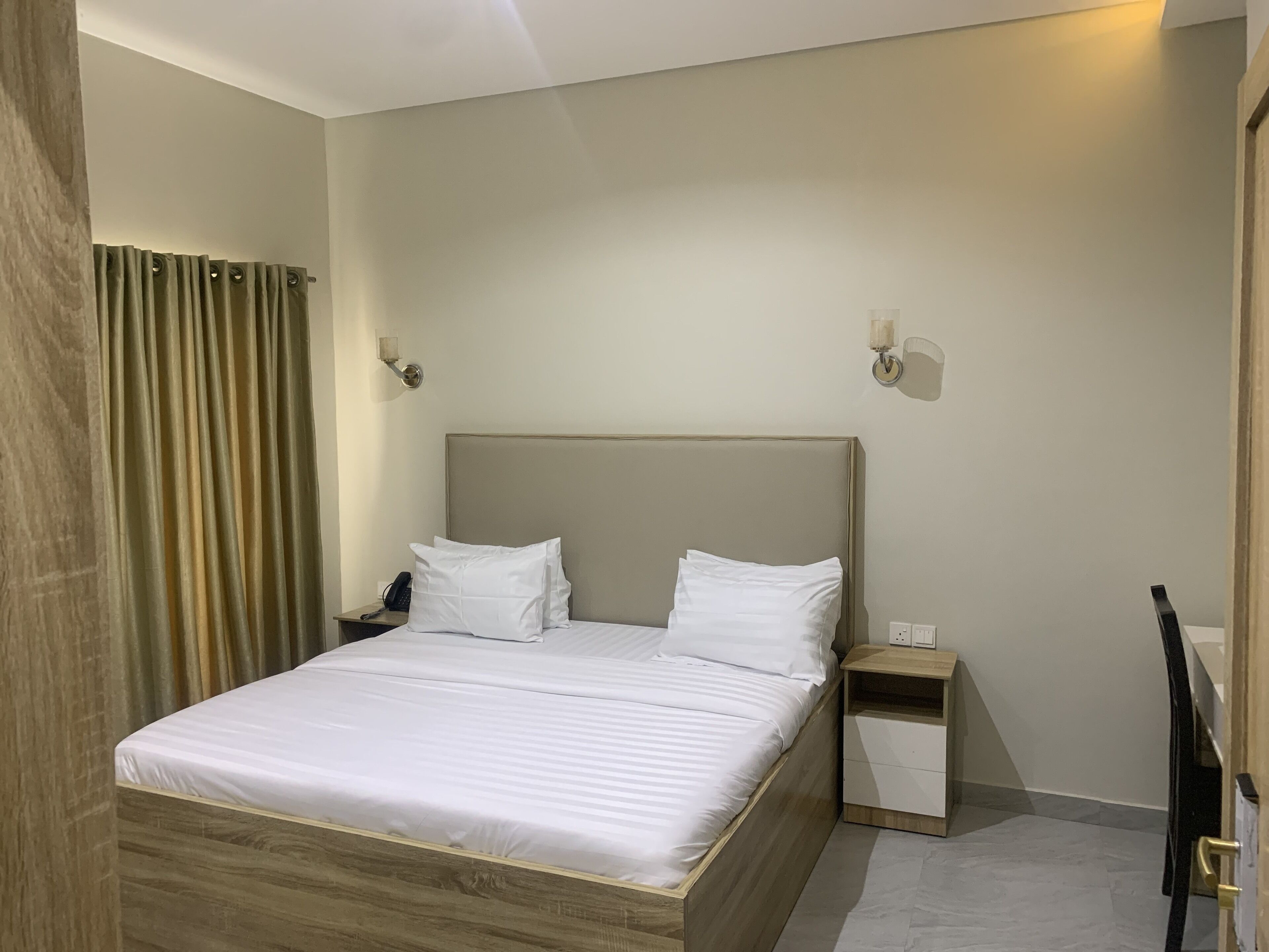 A neatly made bed with white linens and a wooden headboard in a hotel room.