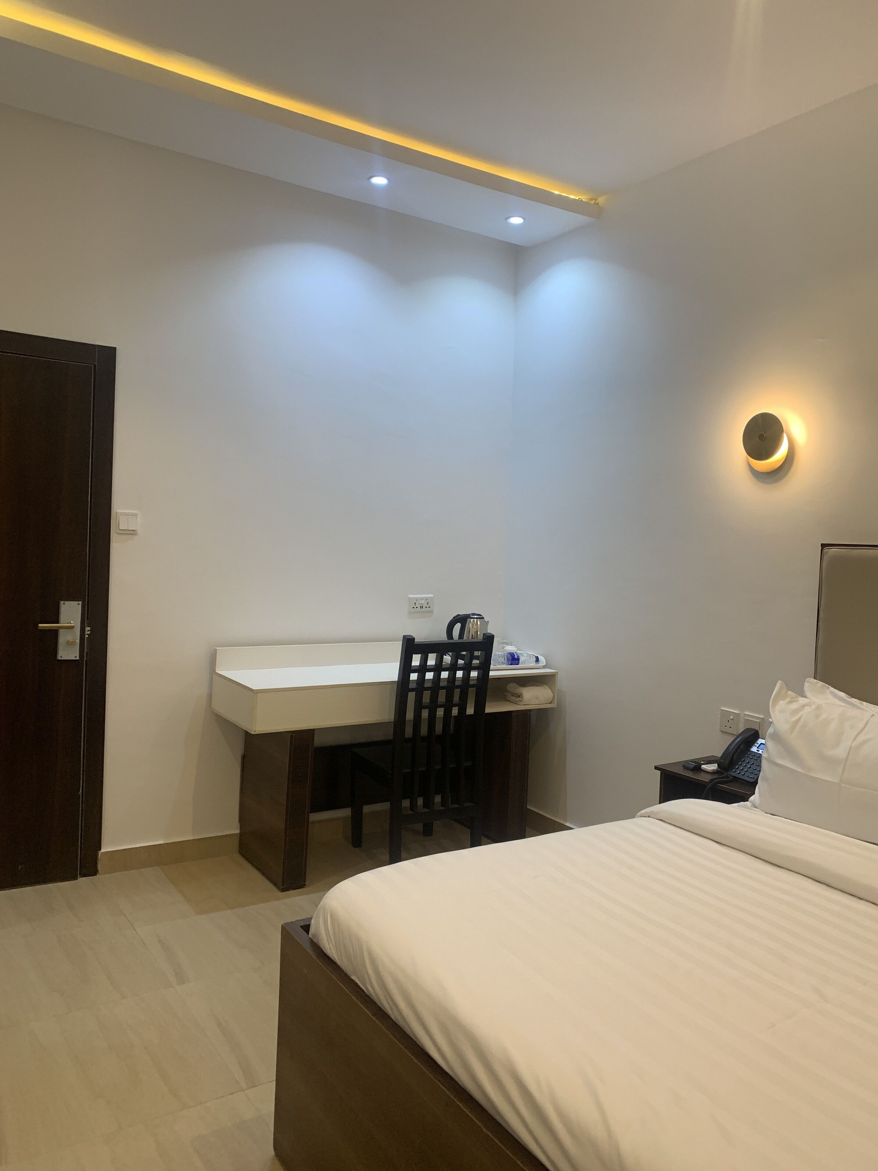 Een hotelkamer met een bed, een bureau, een stoel, een nachtkastje met telefoon en een wandlamp.