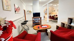 A modern living room with red furniture, a TV on a wooden stand, and a dining area in the background. - Apartments Jezerane (Brinje)