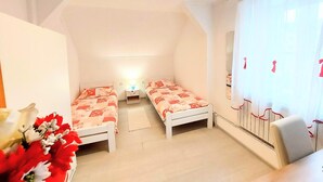 A small, well-lit room with two single beds, a nightstand, and a window with sheer curtains. - Apartments Jezerane (Brinje)