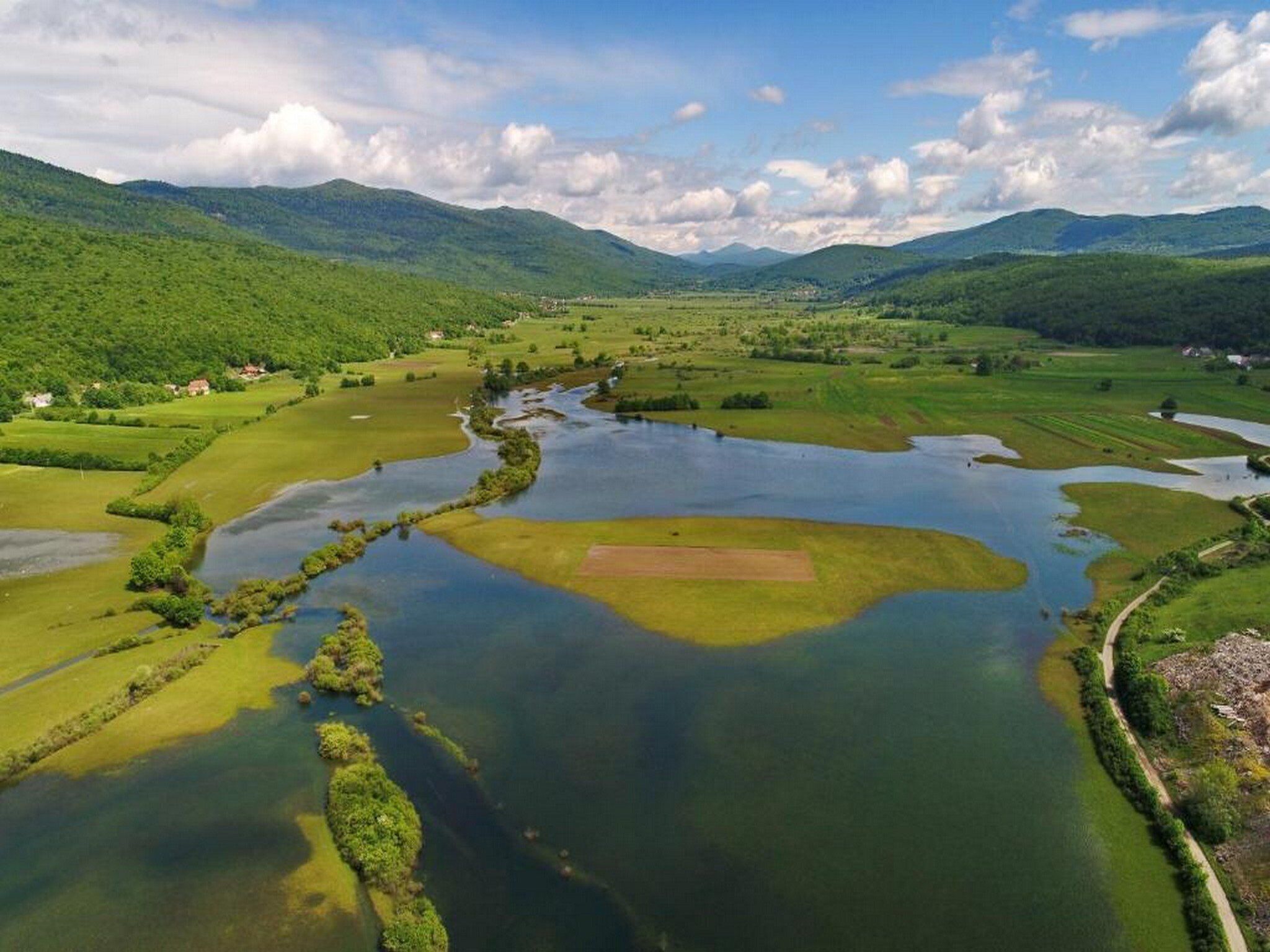 A river winding through a valley with green fields and hills in the background.