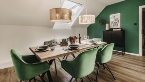 Comedor con mesa de madera dispuesta para cuatro personas, sillas tapizadas en verde e iluminación colgante.