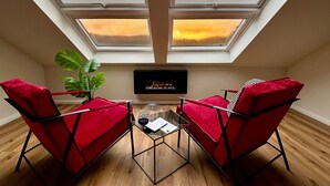 Una habitación acogedora con tragaluz, dos sillas rojas, una mesita de cristal, una planta y un televisor.