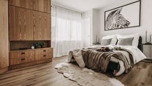 Un dormitorio con un armario de madera, una obra de arte con cebra, una cama con almohadas, una mesita de noche con velas y una alfombra de piel.