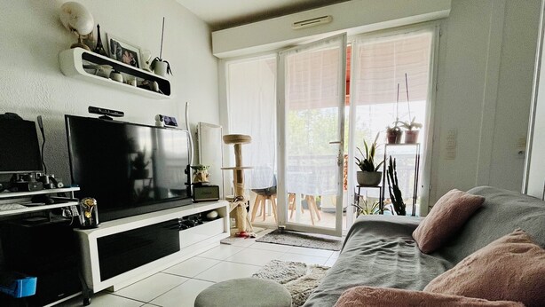 Een moderne woonkamer met een flatscreen televisie, een bank, een salontafel en een schuifpui naar een buitenruimte met planten.