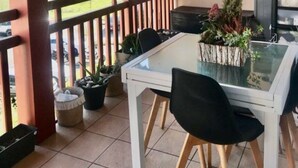 Een overdekt buitengebied met een tafel, stoelen, een leuning en potplanten.