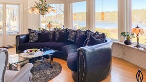 A modern living room with a dark leather sofa, a glass coffee table, and a view of a lake through large windows. - Lovely home in Söderköping with sauna (Söderköping)