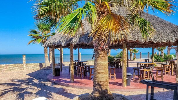 Un restaurante frente a la playa con techos de paja, mesas al aire libre y vistas al océano.