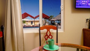 Habitación con vista a una piscina y sombrillas, una silla de madera con una taza verde, y un televisor en la pared.