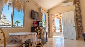 Ein Zimmer mit Esstisch, Stühlen, einem Fernseher und Blick auf den Strand.