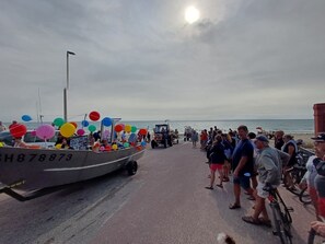 A boat with colorful balloons on a dock, people walking, and a vehicle in the background.
