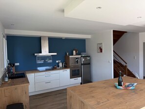 A modern kitchen with white cabinets, a stainless steel range, and a wooden dining table.